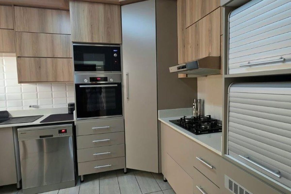 Modern kitchen featuring wood-finish cabinetry, stone countertops, subway tile backsplash, and integrated stainless steel appliances including an oven, microwave, and gas hob.