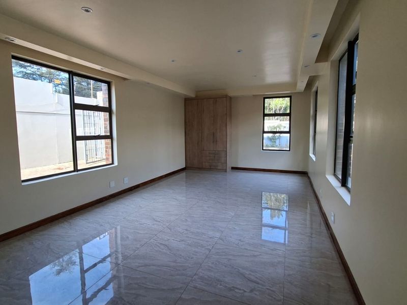 Spacious, empty bedroom featuring modern tiled flooring, built-in cupboards, and large windows that provide ample natural light.