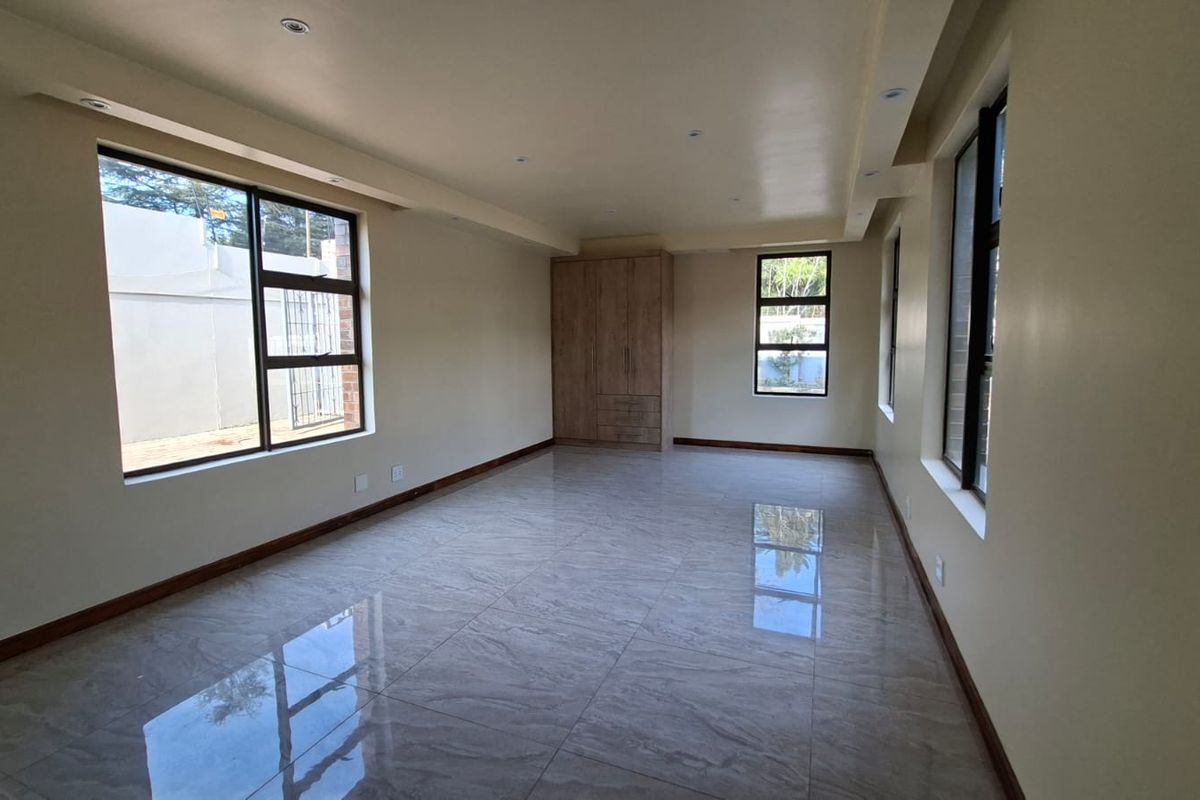 Spacious, empty bedroom featuring modern tiled flooring, built-in cupboards, and large windows that provide ample natural light.