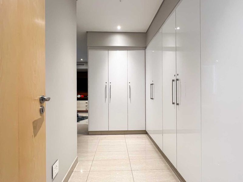 A modern hallway featuring extensive floor-to-ceiling built-in cabinetry with high-gloss white finishes and sleek metal handles, complemented by neutral tiled flooring.