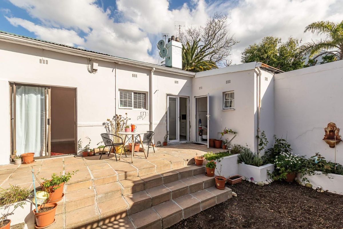 A paved rear patio area featuring a raised terrace, built-in wall fountain, and direct access to the interior living spaces.