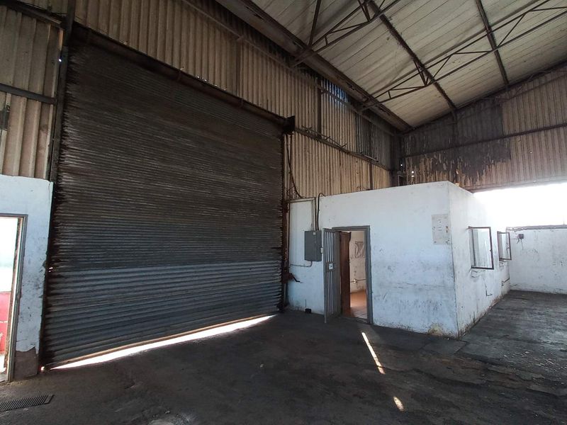 Spacious industrial warehouse featuring high ceilings, a large roller shutter door, and an integrated office or utility room structure.
