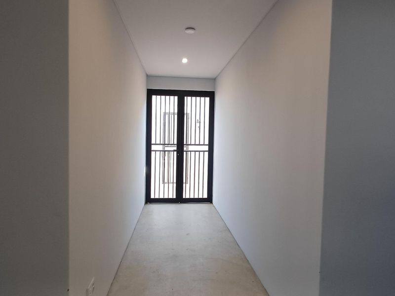 A clean, minimalist hallway featuring smooth walls, recessed lighting, and a secure metal gate entrance.