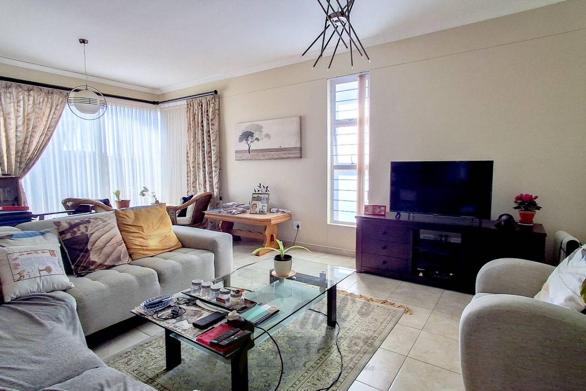 A comfortable living room featuring tiled flooring, large windows with curtains, and a modern light fixture.