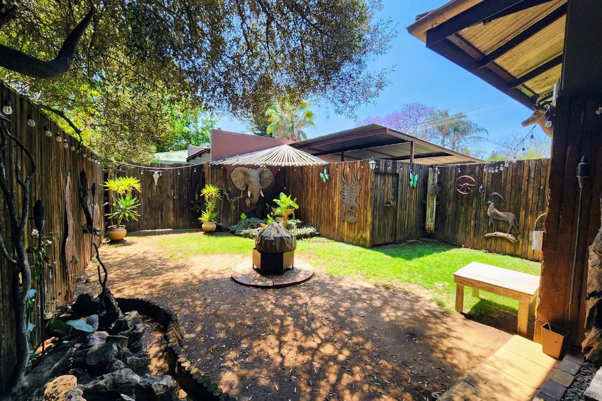 A private rear garden featuring timber fencing, a covered patio area, and a stone water feature, providing a rustic outdoor entertainment space.