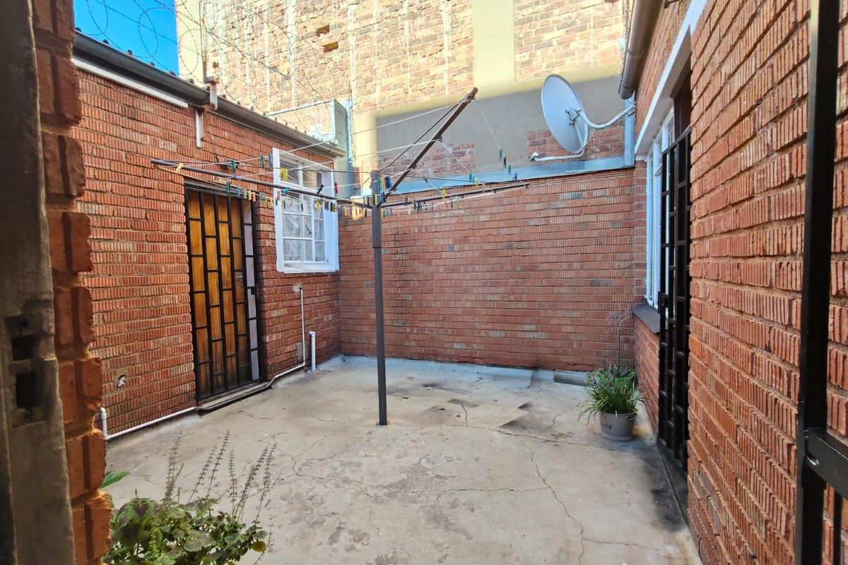 A private rear courtyard area featuring exposed brick walls, concrete paving, and security gates, suitable for utility or outdoor storage use.