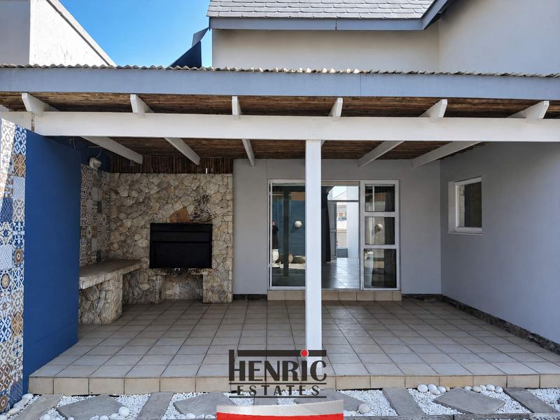 Covered patio area featuring a built-in braai, stone cladding, tiled flooring, and a timber pergola roof, providing seamless access to the interior living space.