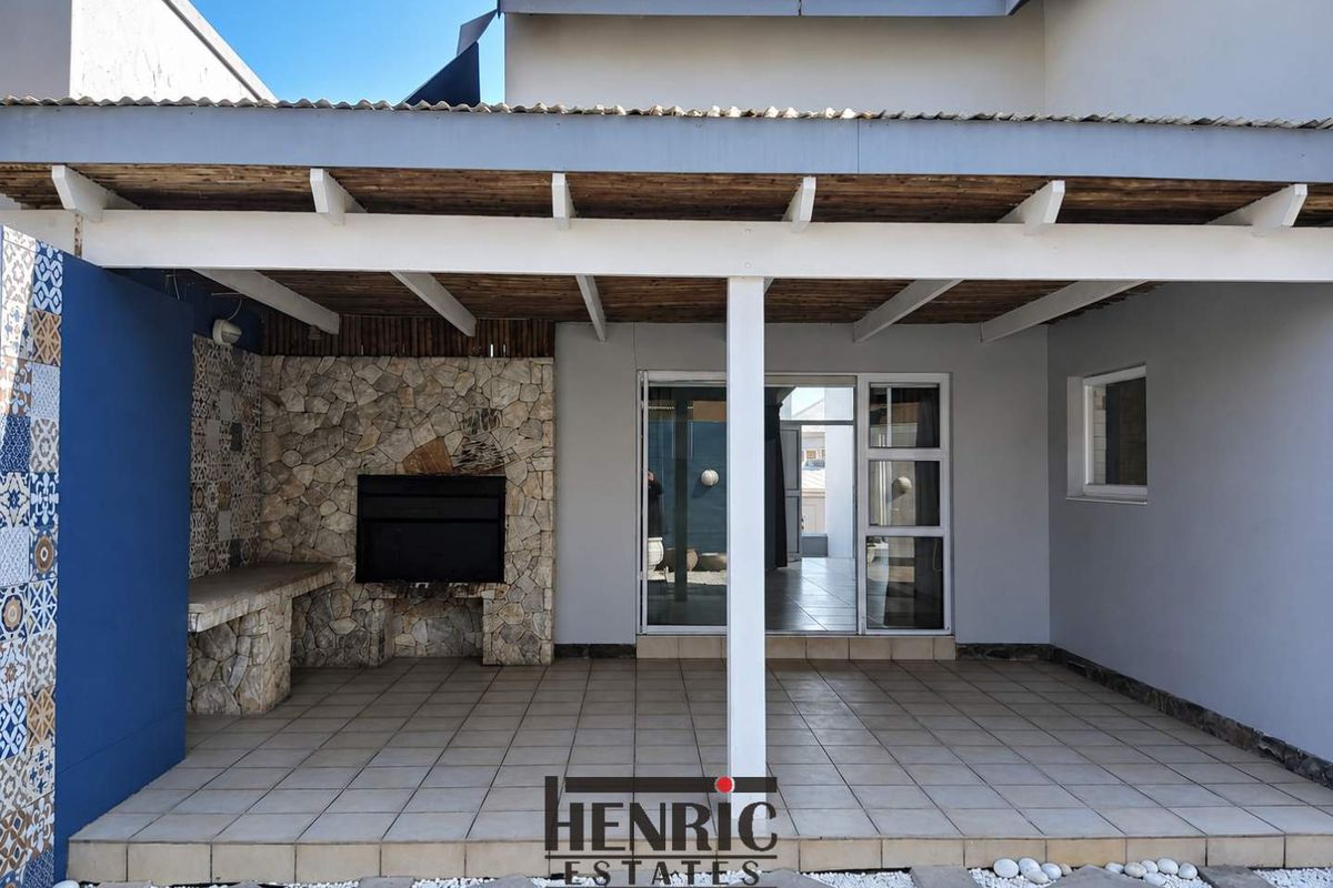 Covered patio area featuring a built-in braai, stone cladding, tiled flooring, and a timber pergola roof, providing seamless access to the interior living space.