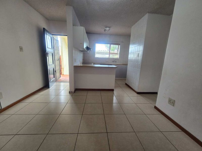 An open-plan living and kitchen area featuring tiled flooring, a breakfast bar, and direct access to an exterior entrance with a security gate.