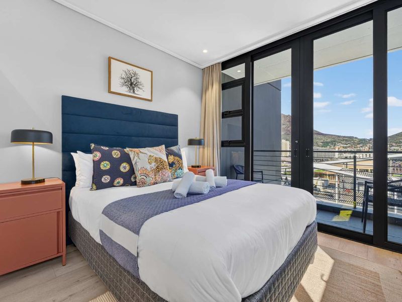 Modern bedroom featuring laminate flooring, recessed lighting, and large sliding glass doors providing direct access to a private balcony with scenic views.