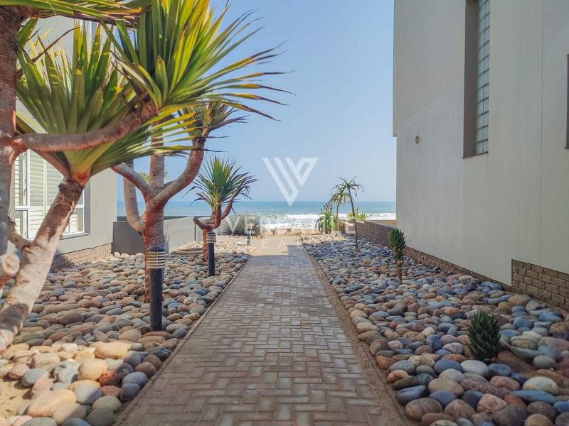 A paved pathway leading through a landscaped pebble garden towards the ocean, providing direct access to the beach from the property.