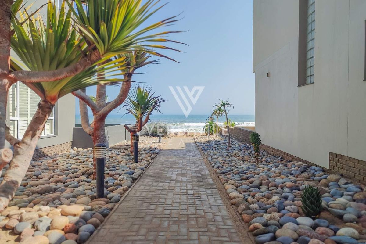 A paved pathway leading through a landscaped pebble garden towards the ocean, providing direct access to the beach from the property.