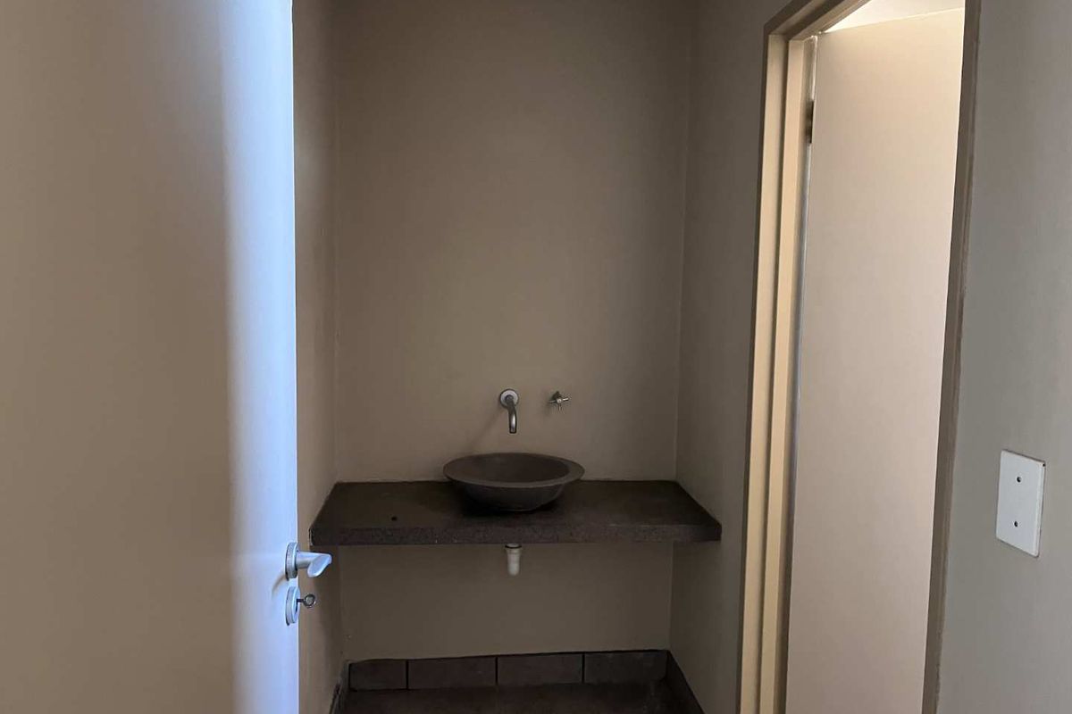 A small washroom area featuring a stone vessel sink mounted on a concrete vanity shelf with tiled flooring.