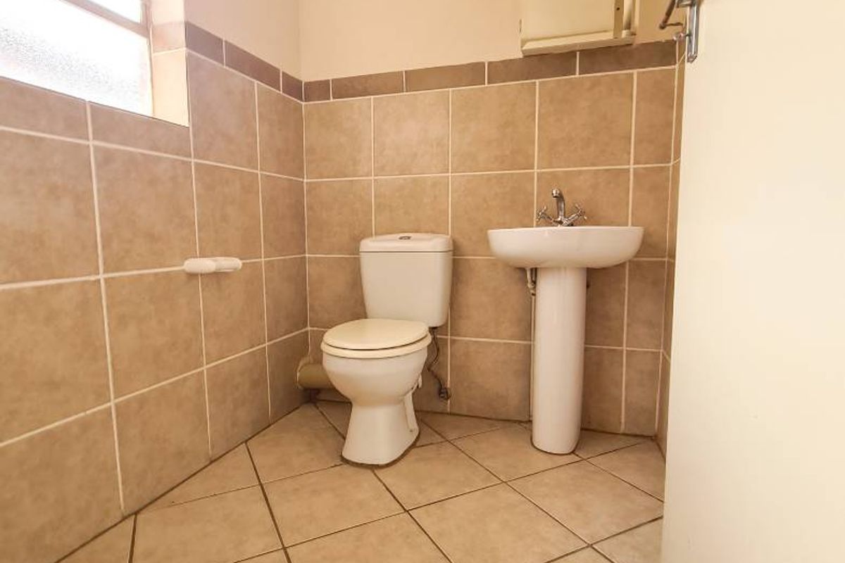 A functional bathroom featuring tiled walls and flooring, a pedestal basin, and a standard toilet, offering a clean and neutral space.