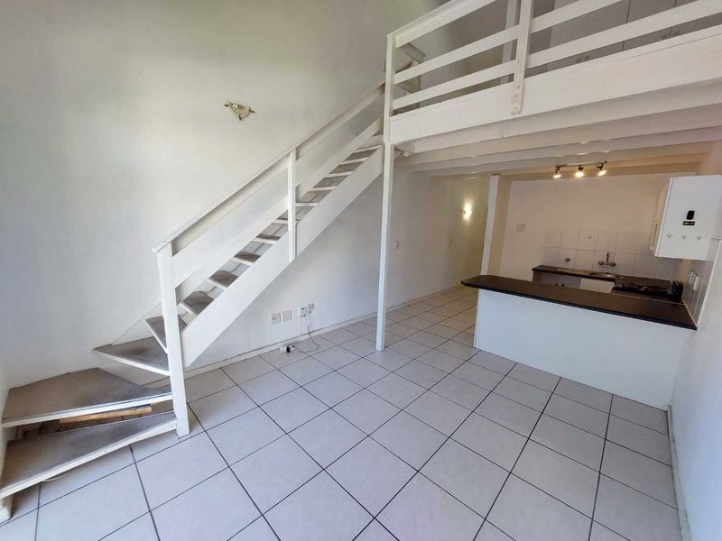 Open-plan living area featuring a mezzanine level, staircase, and a functional kitchen with built-in cabinetry and tiled flooring throughout.