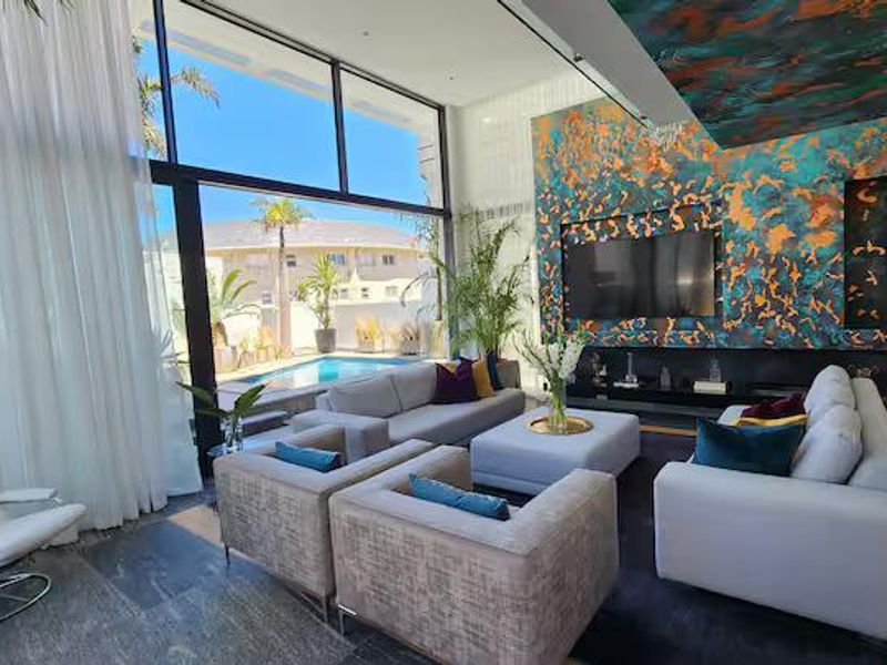 Spacious modern living room featuring floor-to-ceiling windows, a built-in media wall, and seamless access to the outdoor pool area.
