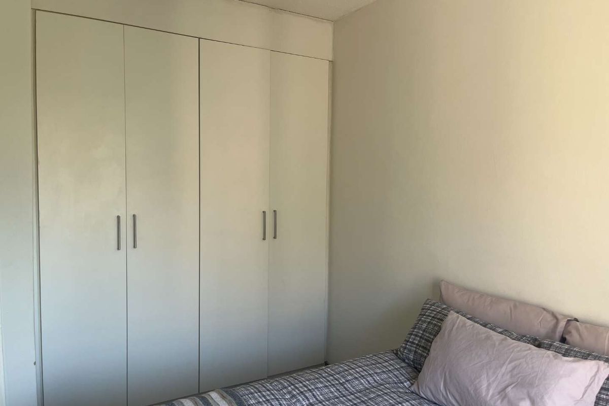 A bedroom featuring a floor-to-ceiling built-in wardrobe with white doors and modern handles.