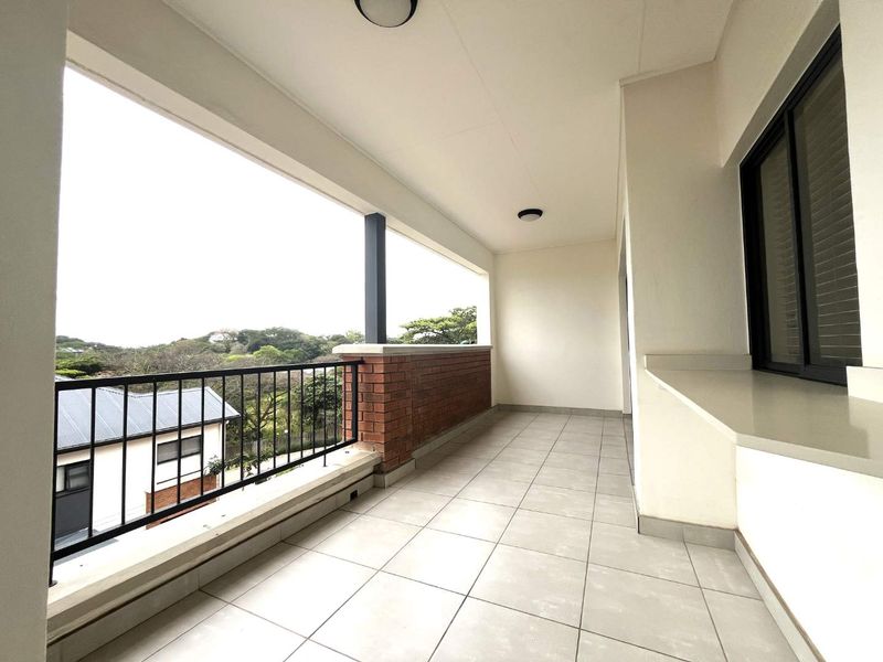 A spacious covered balcony featuring tiled flooring, a brick balustrade with metal railing, and a convenient built-in counter, offering pleasant outdoor views.