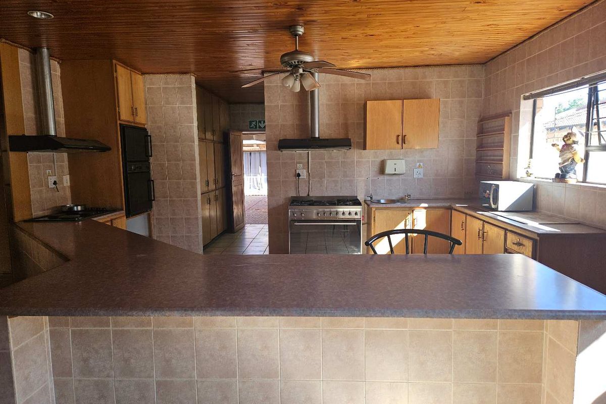 A functional kitchen featuring a breakfast bar, built-in oven and hob, extractor fans, and tiled splashbacks with a wooden panel ceiling.