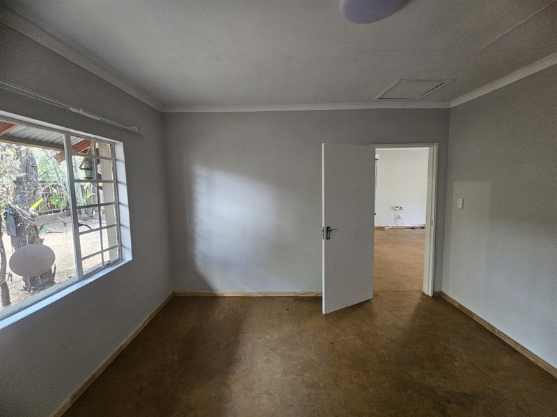 A vacant bedroom featuring neutral walls, polished concrete-style flooring, and a steel-framed window with security bars.
