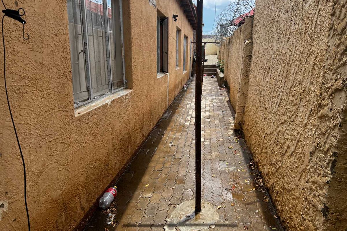 A narrow side passage featuring paved flooring, textured exterior walls, and a fixed metal washing line structure.