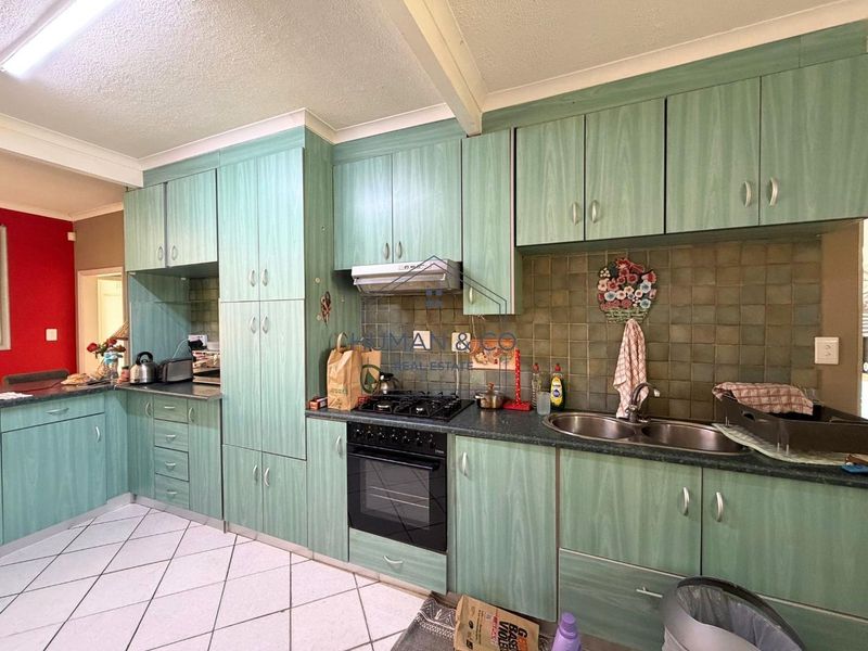 A functional kitchen featuring green laminate cabinetry, a gas hob with extractor, double stainless steel sink, and tiled flooring.
