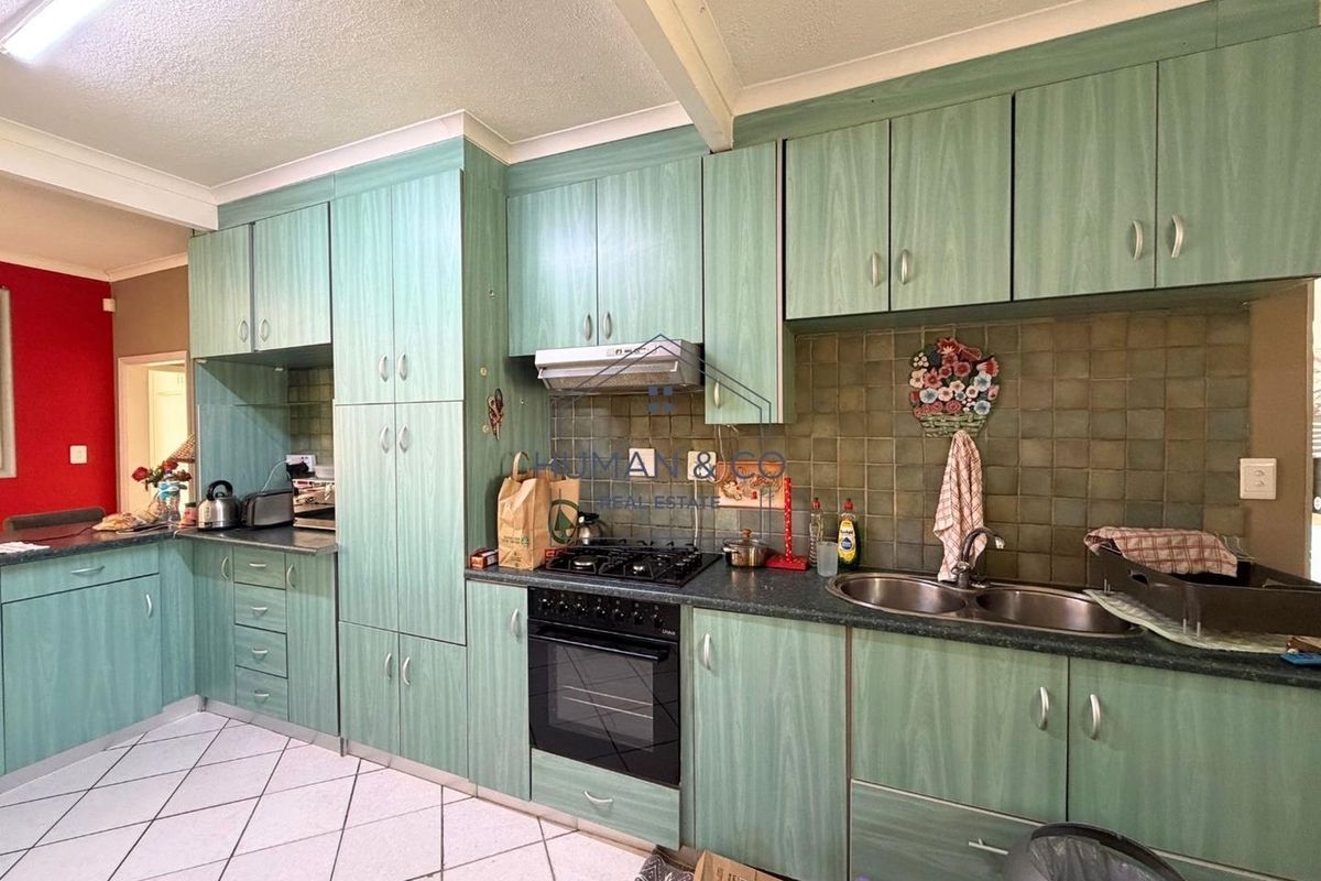 A functional kitchen featuring green laminate cabinetry, a gas hob with extractor, double stainless steel sink, and tiled flooring.