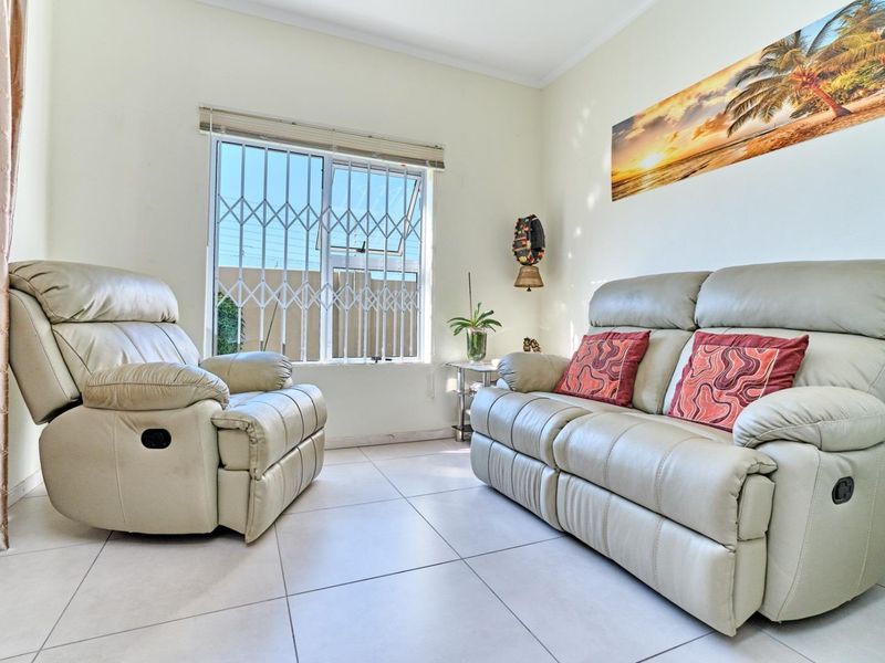 A bright living room featuring neutral tiled flooring and a window fitted with a security gate, offering a functional and well-lit space.