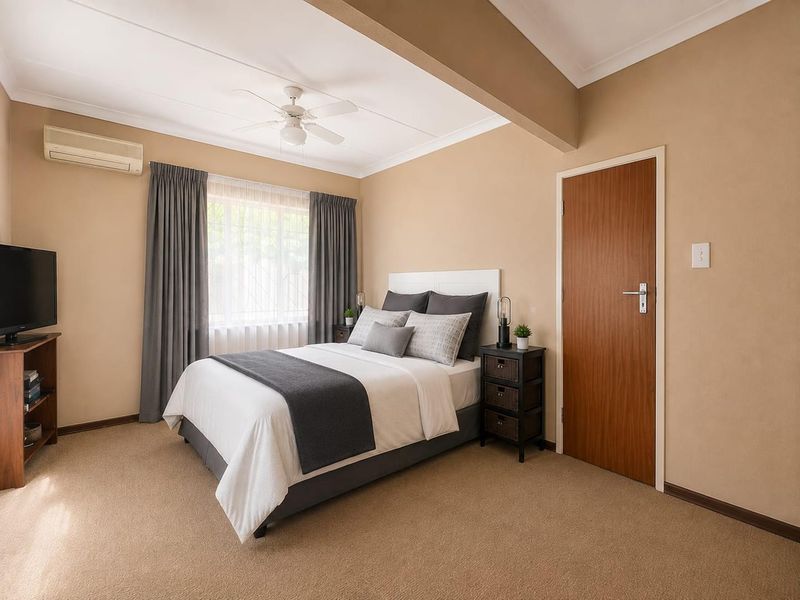A well-maintained bedroom featuring neutral wall tones, carpet flooring, a ceiling fan, and a split-system air conditioner for climate control.
