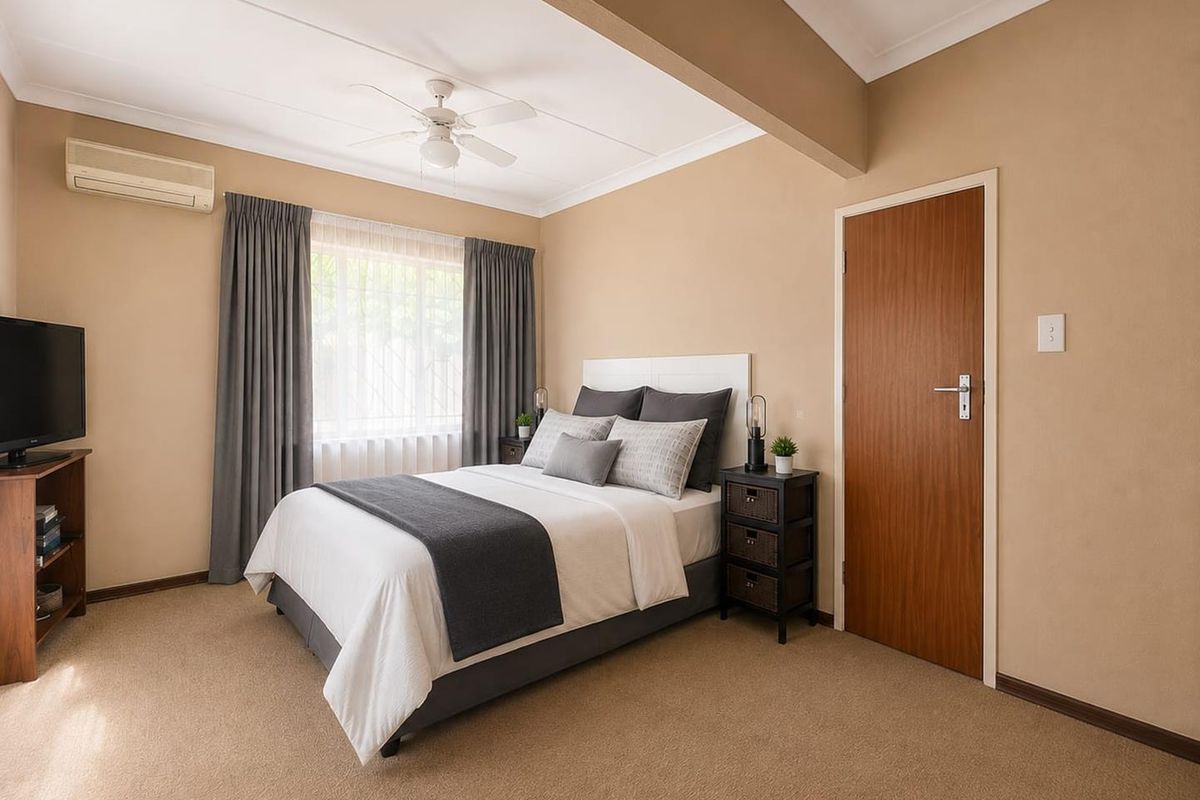 A well-maintained bedroom featuring neutral wall tones, carpet flooring, a ceiling fan, and a split-system air conditioner for climate control.