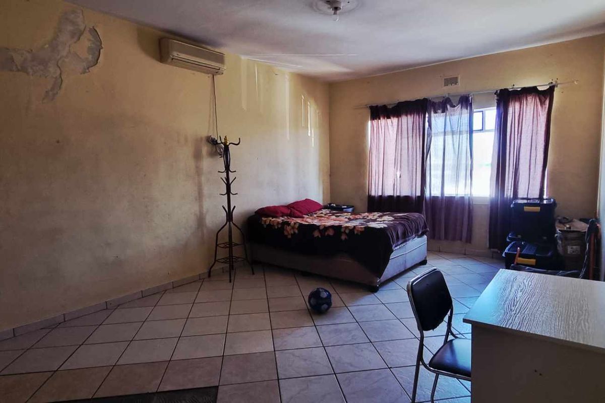 A bedroom featuring tiled flooring, a wall-mounted air conditioning unit, and large windows with curtains, requiring cosmetic updates to the wall finishes.