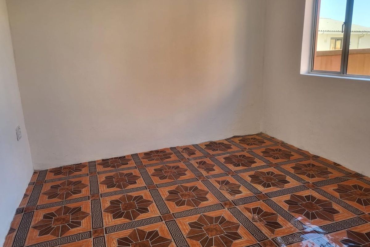 An empty bedroom featuring patterned ceramic floor tiles and a single window, providing a blank canvas for potential interior design updates.