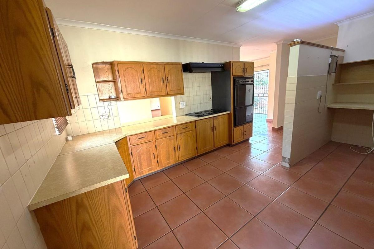 A functional kitchen featuring wooden cabinetry, built-in oven, hob, extractor fan, and tiled flooring, offering a practical layout with potential for modernization.