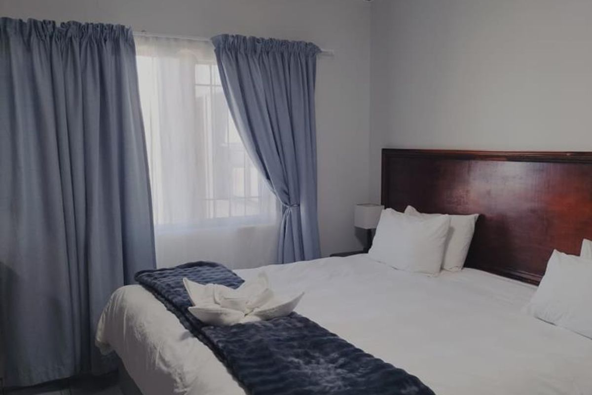 A bedroom featuring tiled flooring, a built-in wooden headboard, and window curtains.