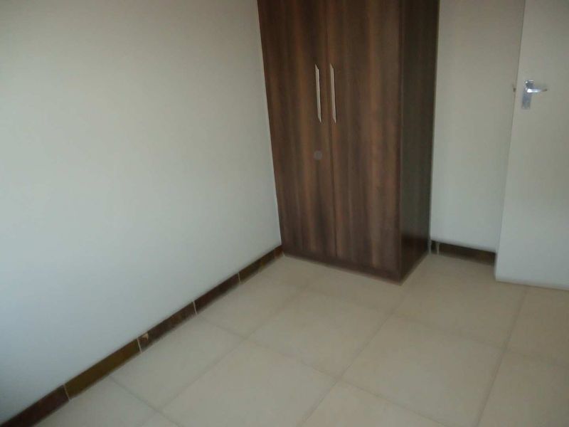 A compact, empty bedroom featuring neutral tiled flooring and a built-in wooden wardrobe.