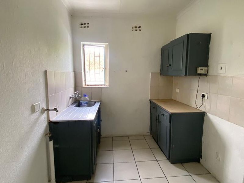A functional scullery or utility area featuring tiled flooring, built-in cabinetry, a stainless steel sink, and tiled splashbacks.