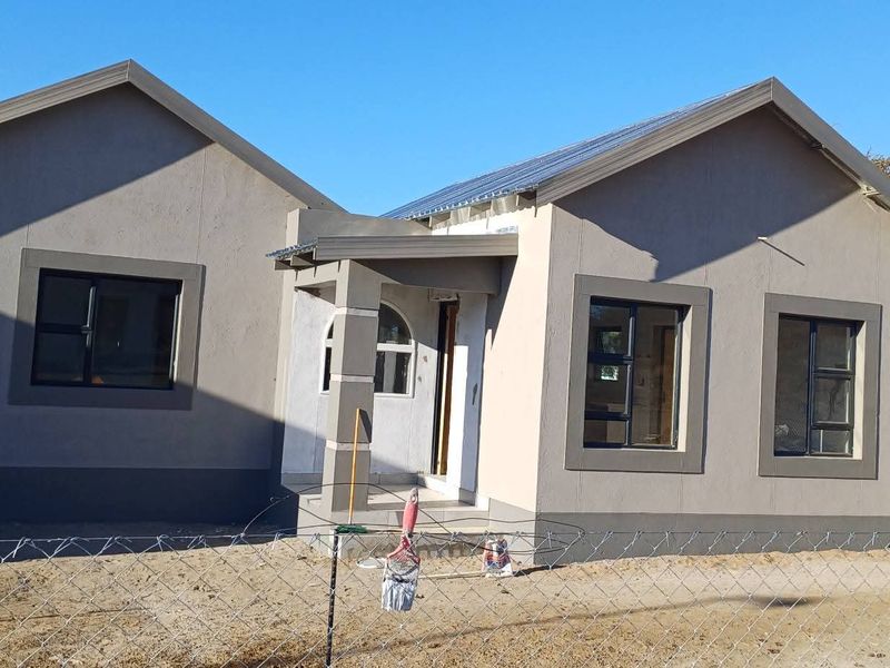 Front view of a modern single-story house featuring a dual-gable roof design, plastered exterior walls, and aluminium window frames.