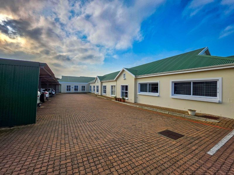 Exterior view of a retirement village complex featuring a paved driveway, covered parking bays, and well-maintained building facades with green metal roofing.