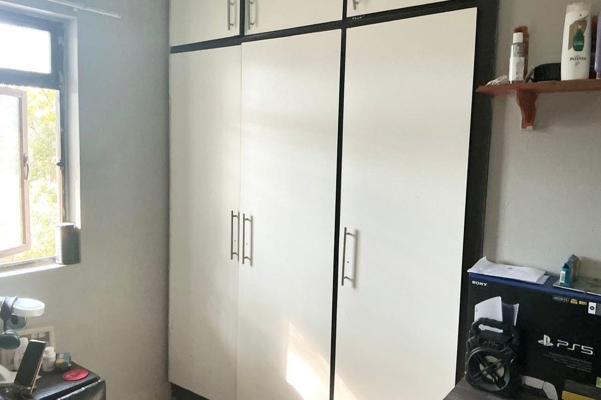 A bedroom featuring white built-in cupboards with dark trim and a window providing natural light.