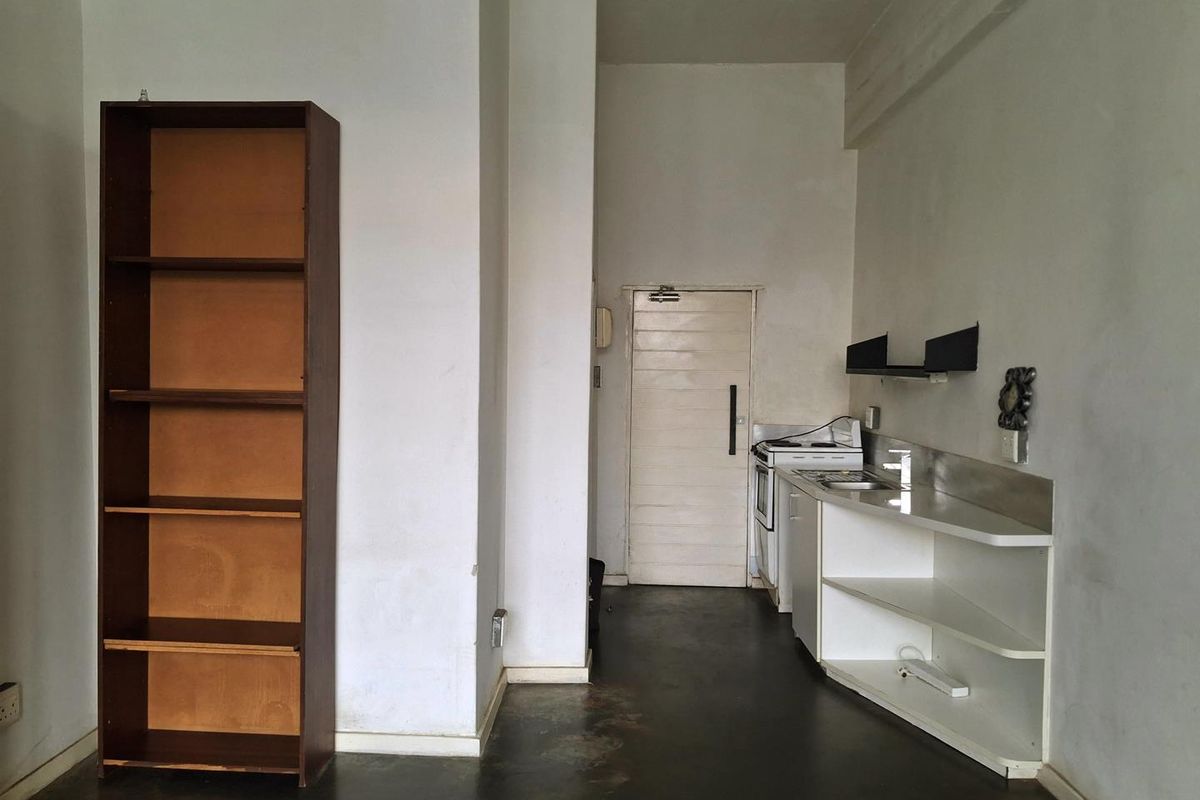 A compact kitchen area featuring basic cabinetry, a freestanding stove, and a sink, set within an open-plan living space with concrete flooring.