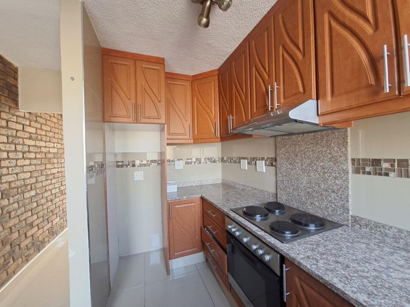 A functional kitchen featuring wooden cabinetry, granite countertops, a built-in oven with hob, and an attractive exposed brick feature wall in the adjacent area.