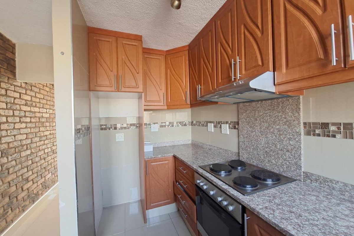 A functional kitchen featuring wooden cabinetry, granite countertops, a built-in oven with hob, and an attractive exposed brick feature wall in the adjacent area.