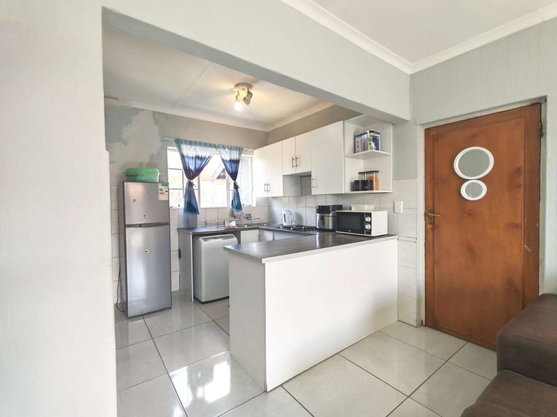 Open plan kitchen featuring white cabinetry, laminate countertops, and tiled flooring, with direct access to the living area.