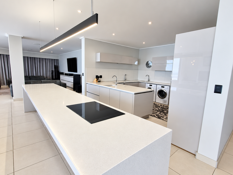 Modern open-plan kitchen featuring a large central island with integrated hob, sleek cabinetry, and high-quality finishes, seamlessly flowing into the living area.