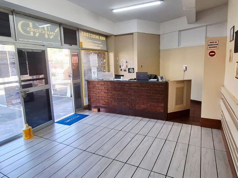 Commercial reception area featuring a brick-fronted service desk, tiled flooring, and large glass entrance doors providing natural light.