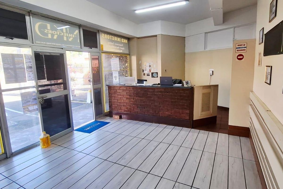 Commercial reception area featuring a brick-fronted service desk, tiled flooring, and large glass entrance doors providing natural light.