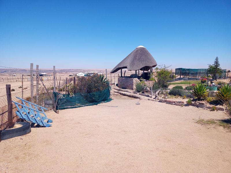 Outdoor area featuring a traditional thatch lapa structure, open sandy ground, and perimeter wire fencing in a rural small holding setting.