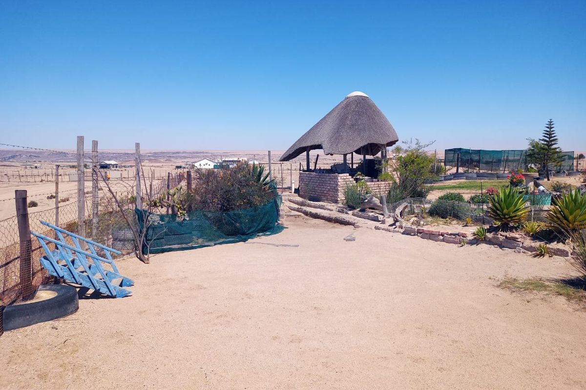 Outdoor area featuring a traditional thatch lapa structure, open sandy ground, and perimeter wire fencing in a rural small holding setting.