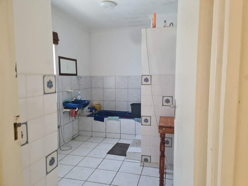 A dated bathroom featuring tiled walls and flooring, a built-in bathtub, and a wall-mounted basin, offering potential for a modern renovation.