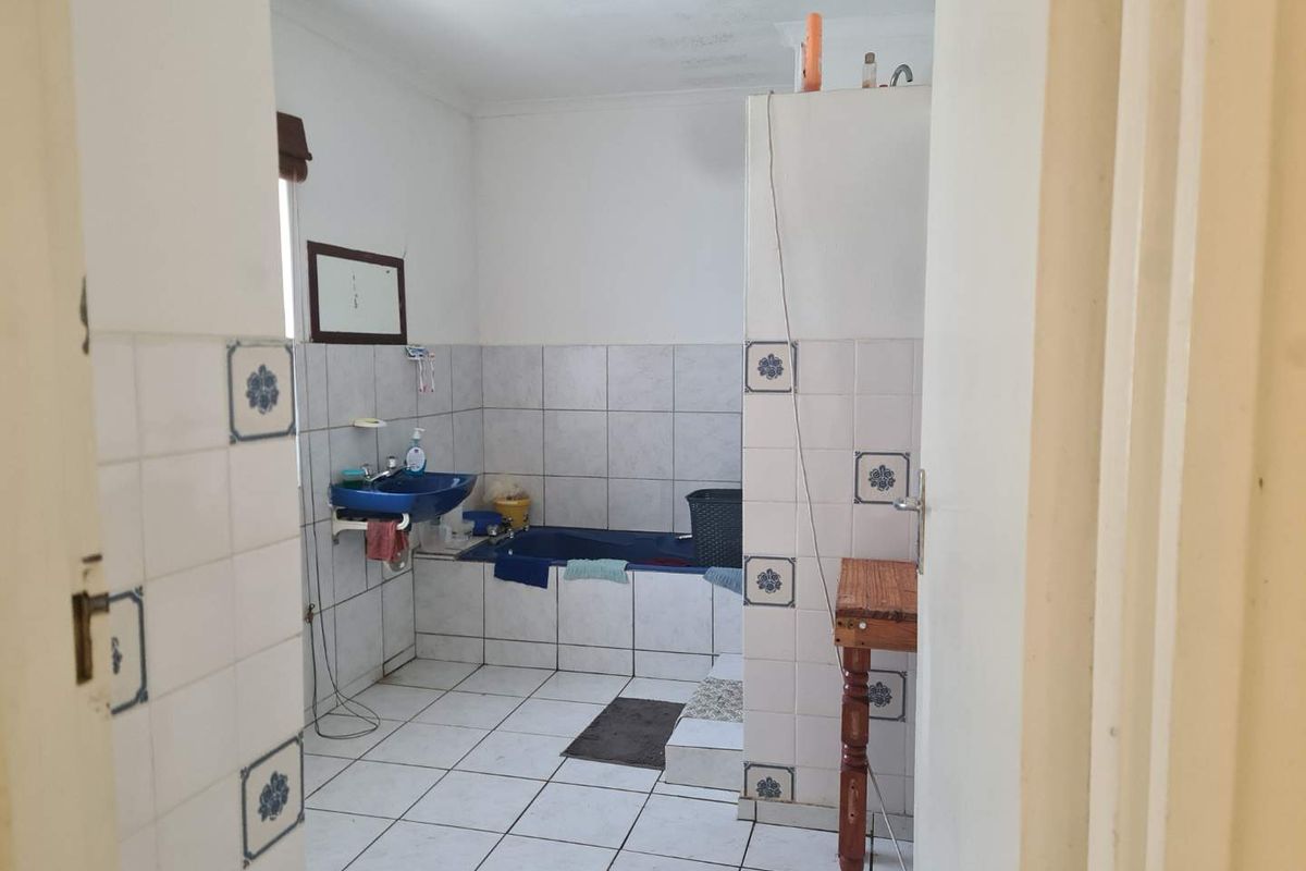 A dated bathroom featuring tiled walls and flooring, a built-in bathtub, and a wall-mounted basin, offering potential for a modern renovation.
